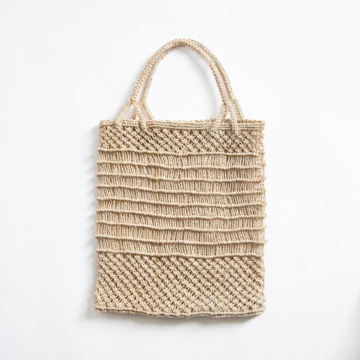 A beige raffia tote bag hanging on a white surface.