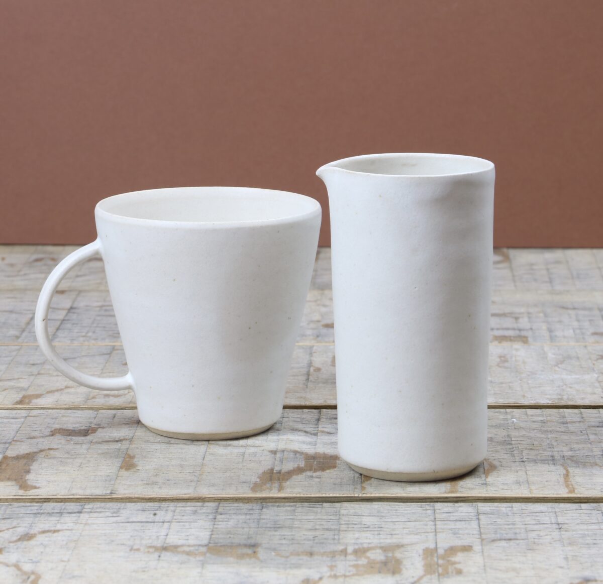 Two white Everyday cups and a pitcher on a wooden table.