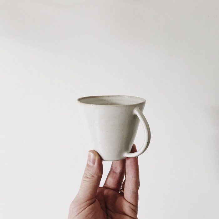 A person holding up a small cup on a white background.