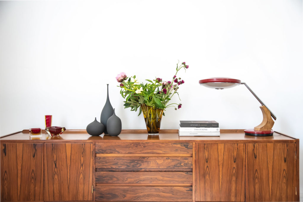 A wooden sideboard with a vase and a lamp.