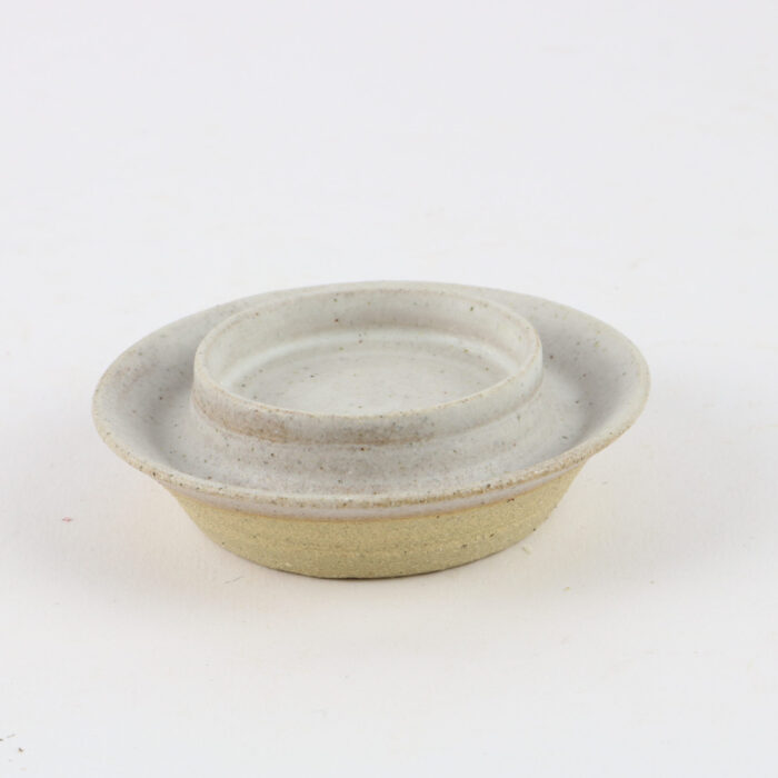 A small bowl with a lid sitting on a white surface.